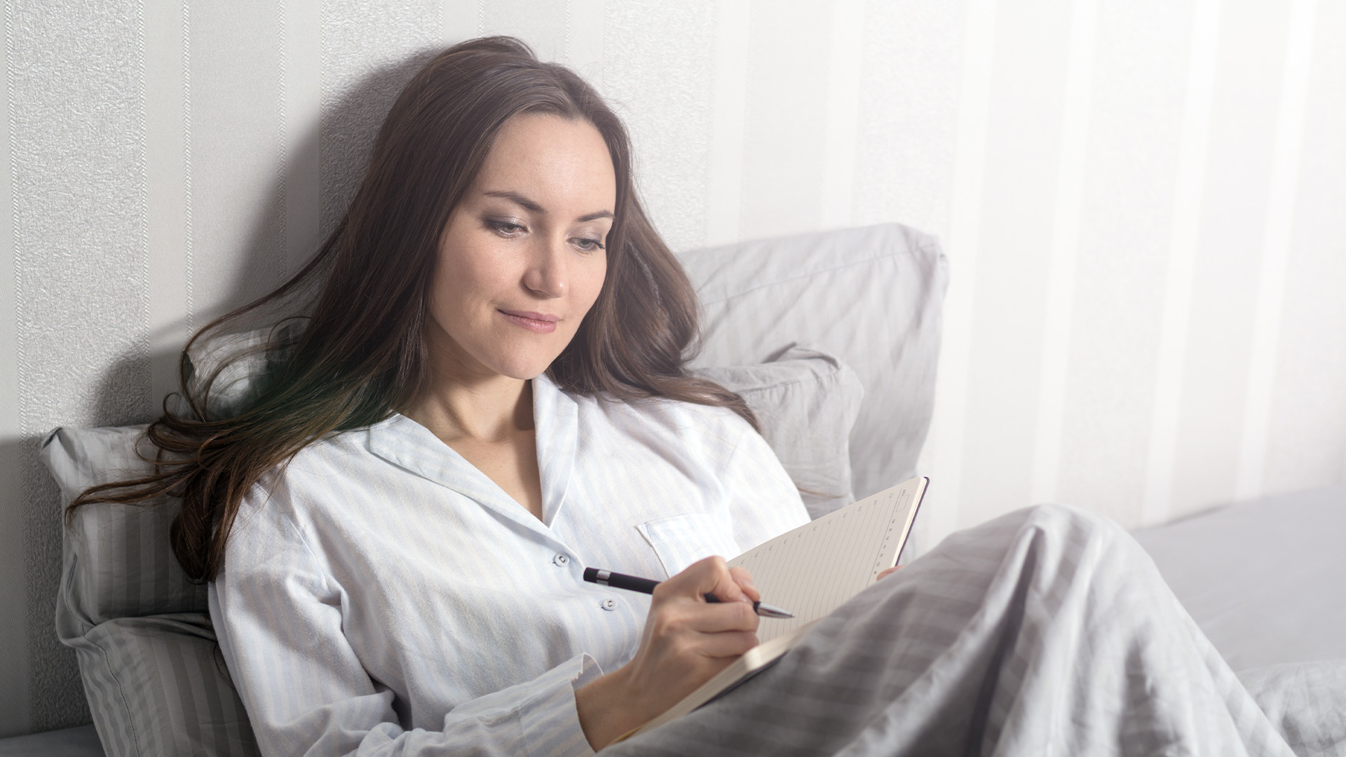 Woman laying in bed in pajamas, writing in notebook