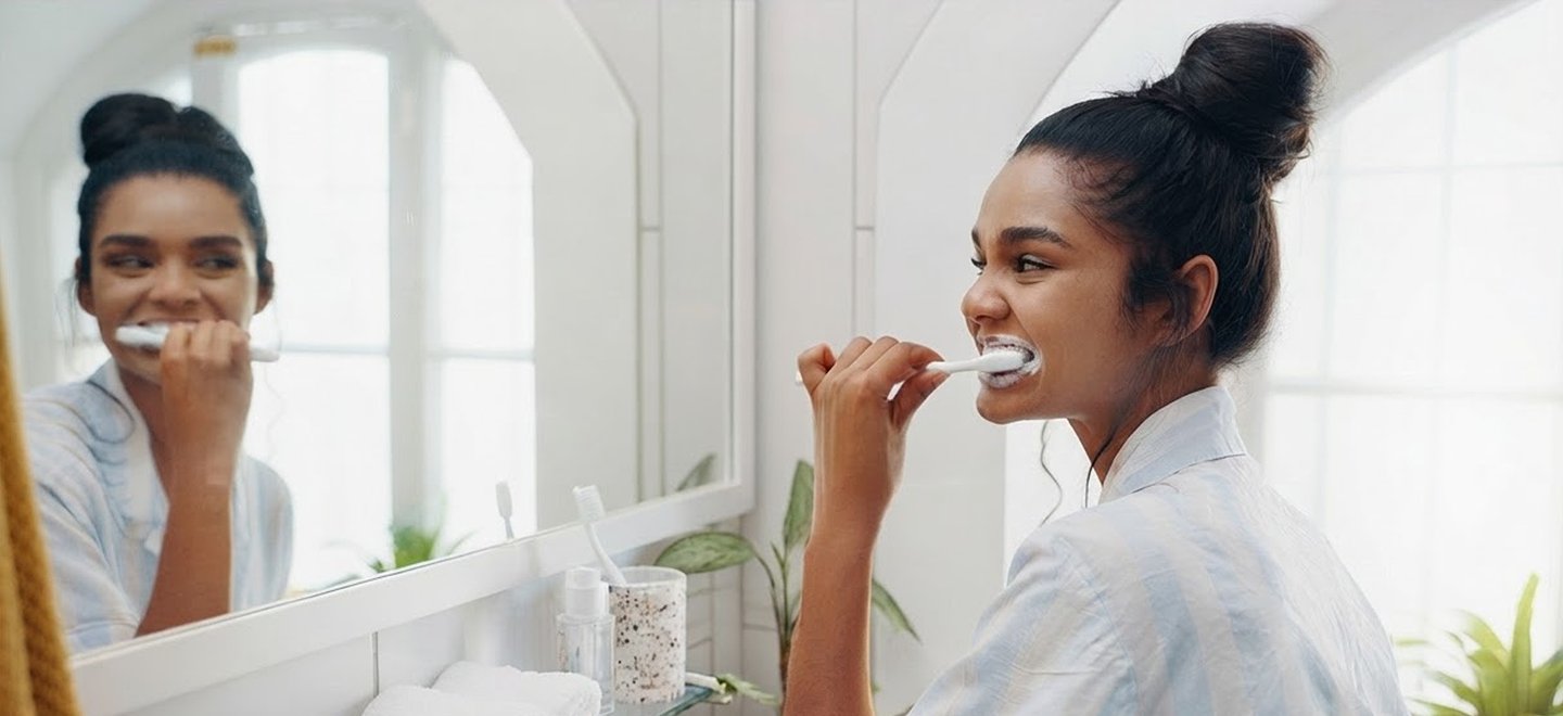Woman smiling while brushing her teeth in a bright bathroom