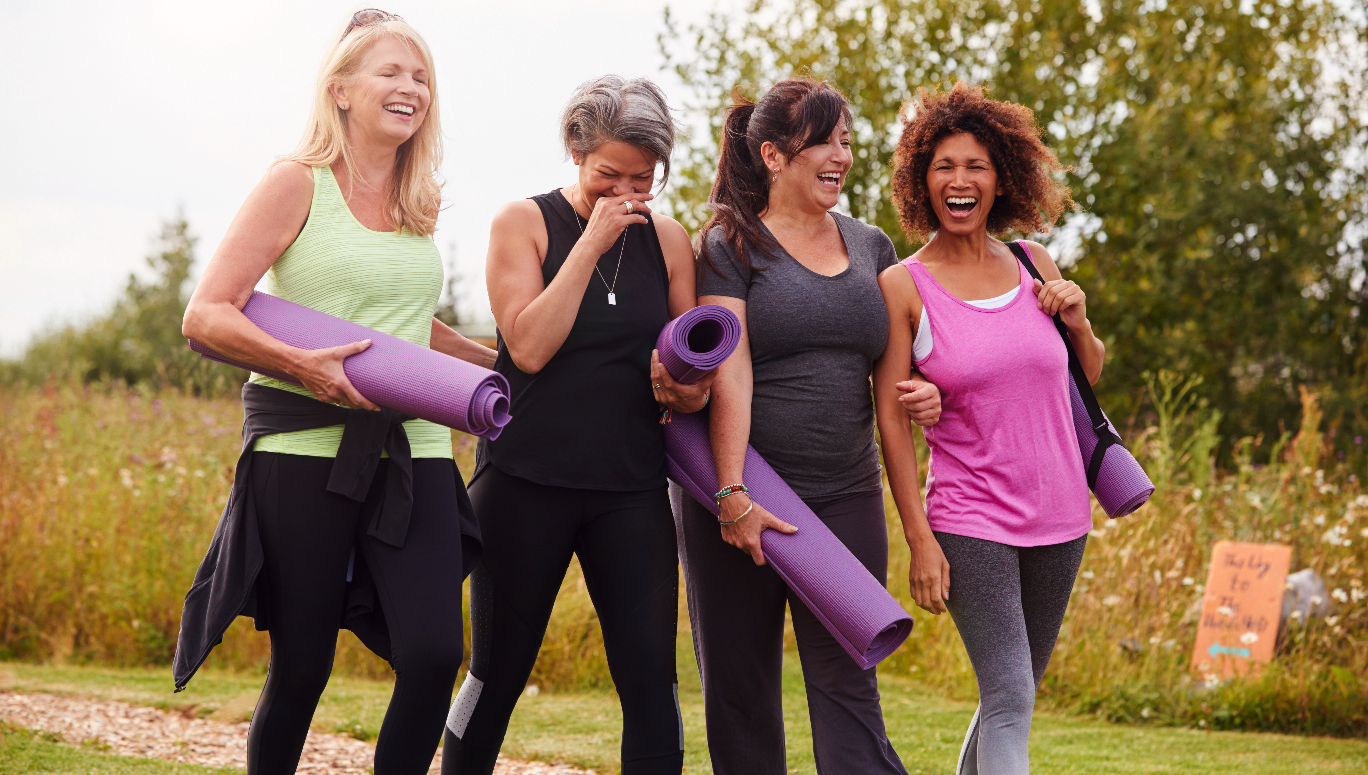 Four women smiling while walking and holding yoga mats