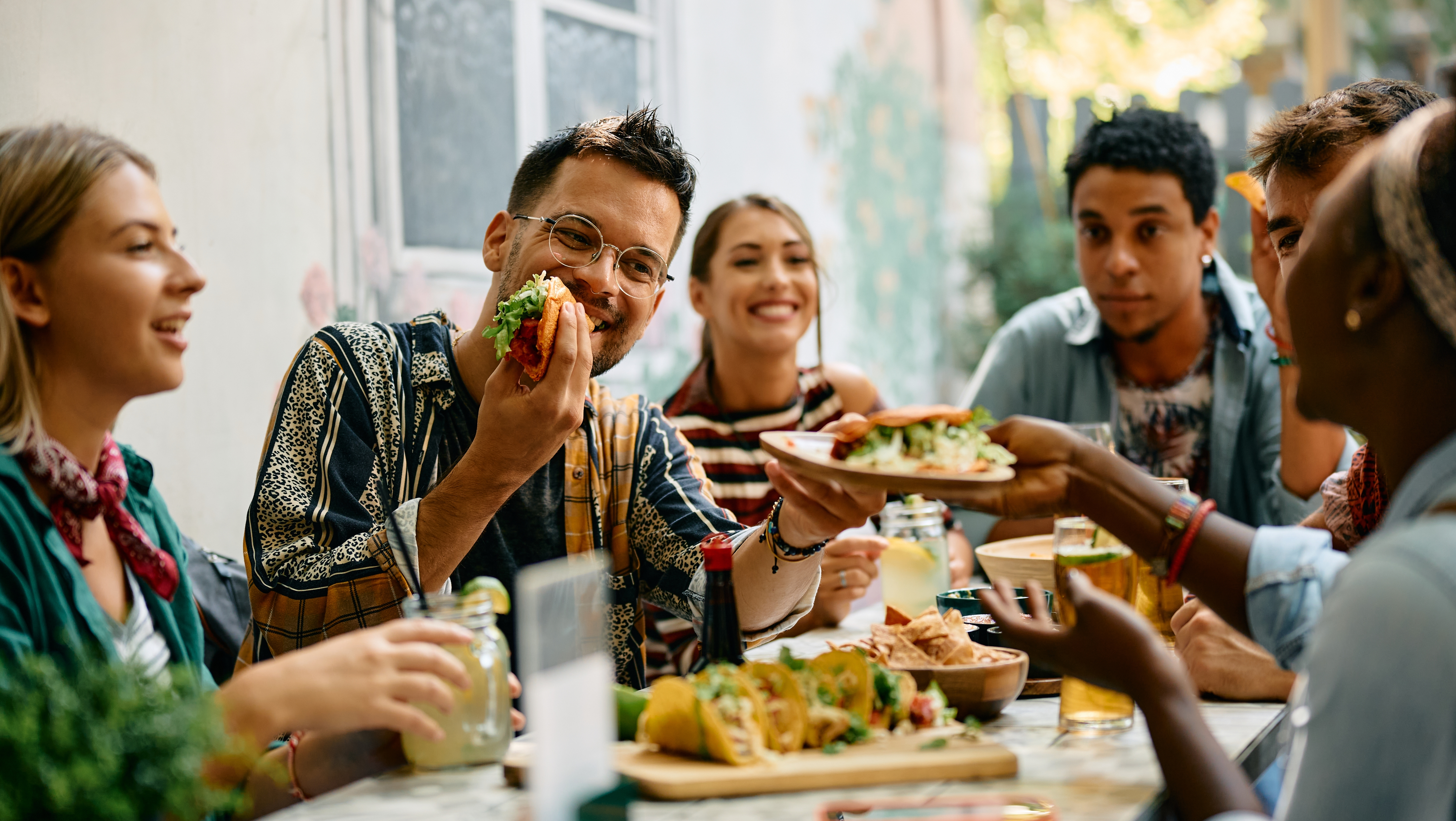Group of friends having fun and eating tacos together on an outdoor patio