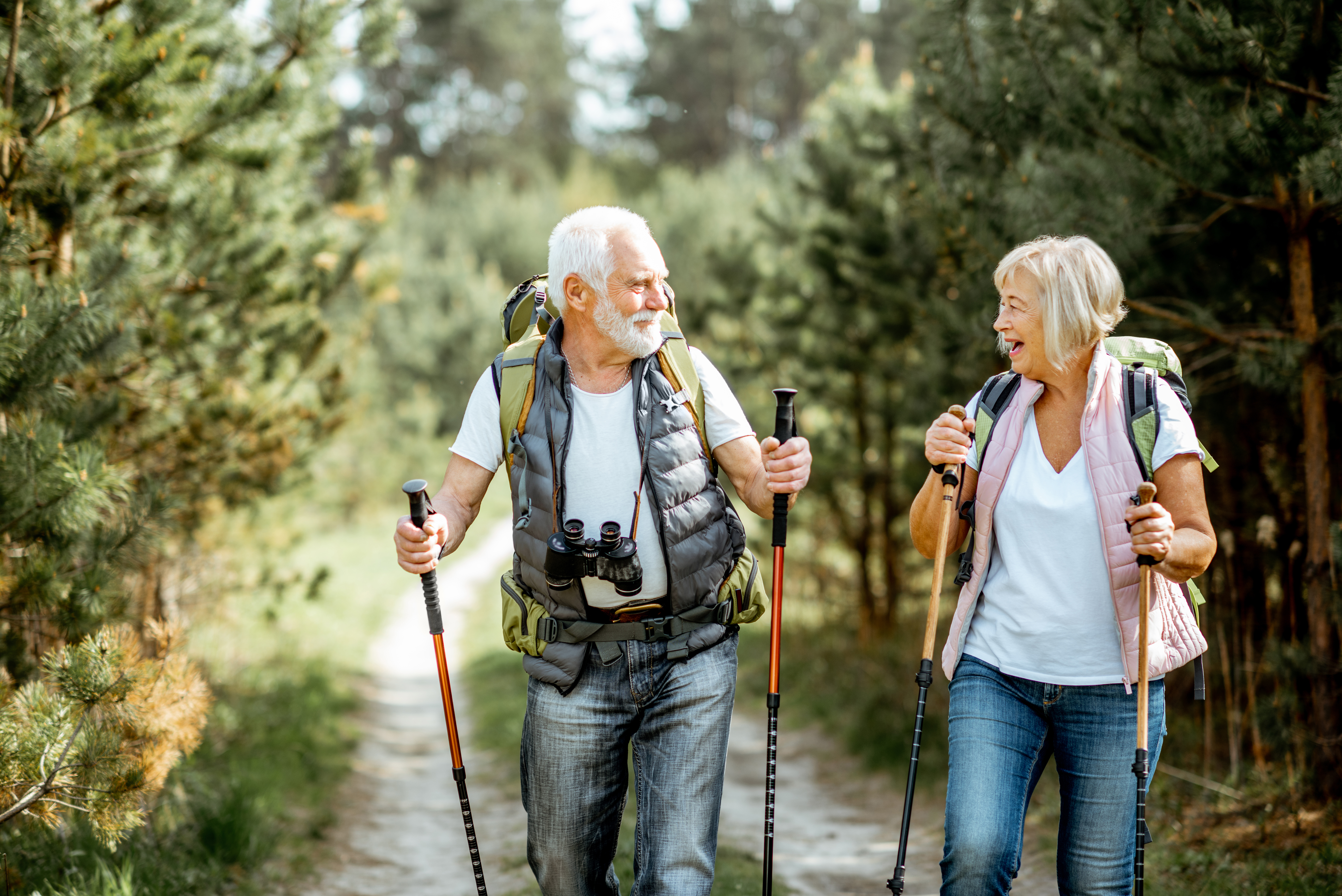 Happy older couple smiling while hiking with their trekking sticks and
backpacks through a forest