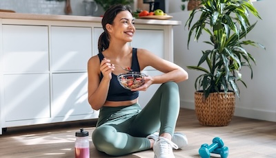 Athletic woman eating a healthy bowl of fruit sitting on floor in the kitchen at home.